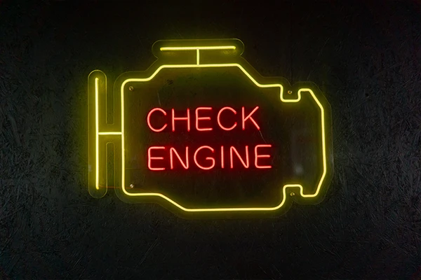 An illuminated neon sign in the shape of a check engine warning light with the words "check engine" glowing in the middle